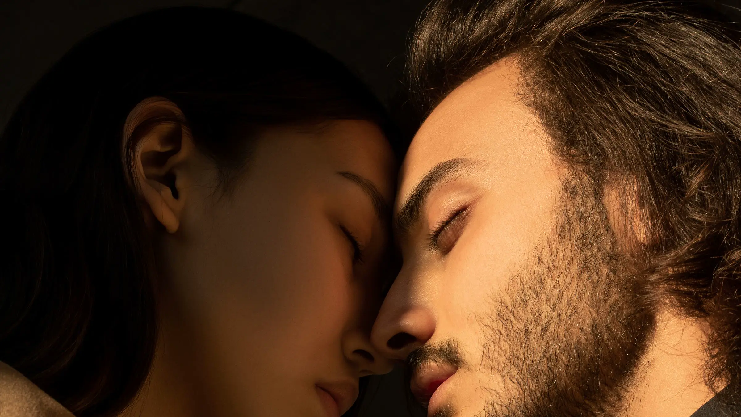 Una pareja en penumbra, frente con frente y con los ojos cerrados.