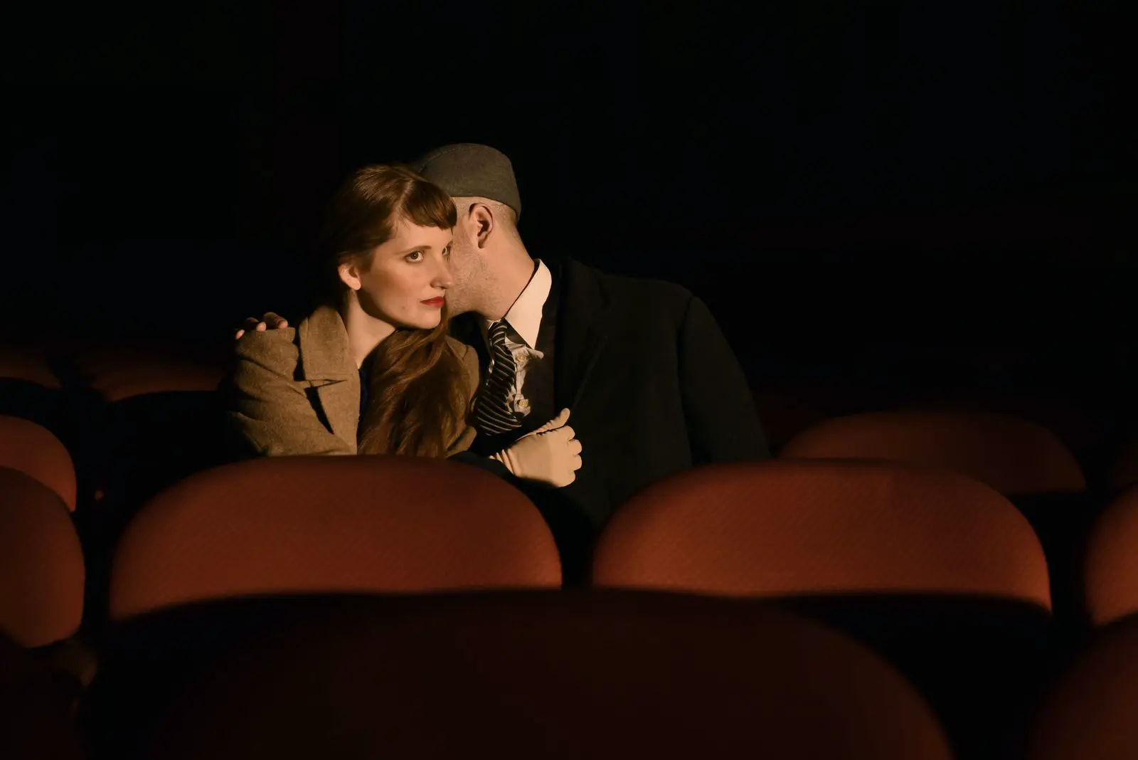 Una pareja conversa en voz baja en la butaca de un teatro.
